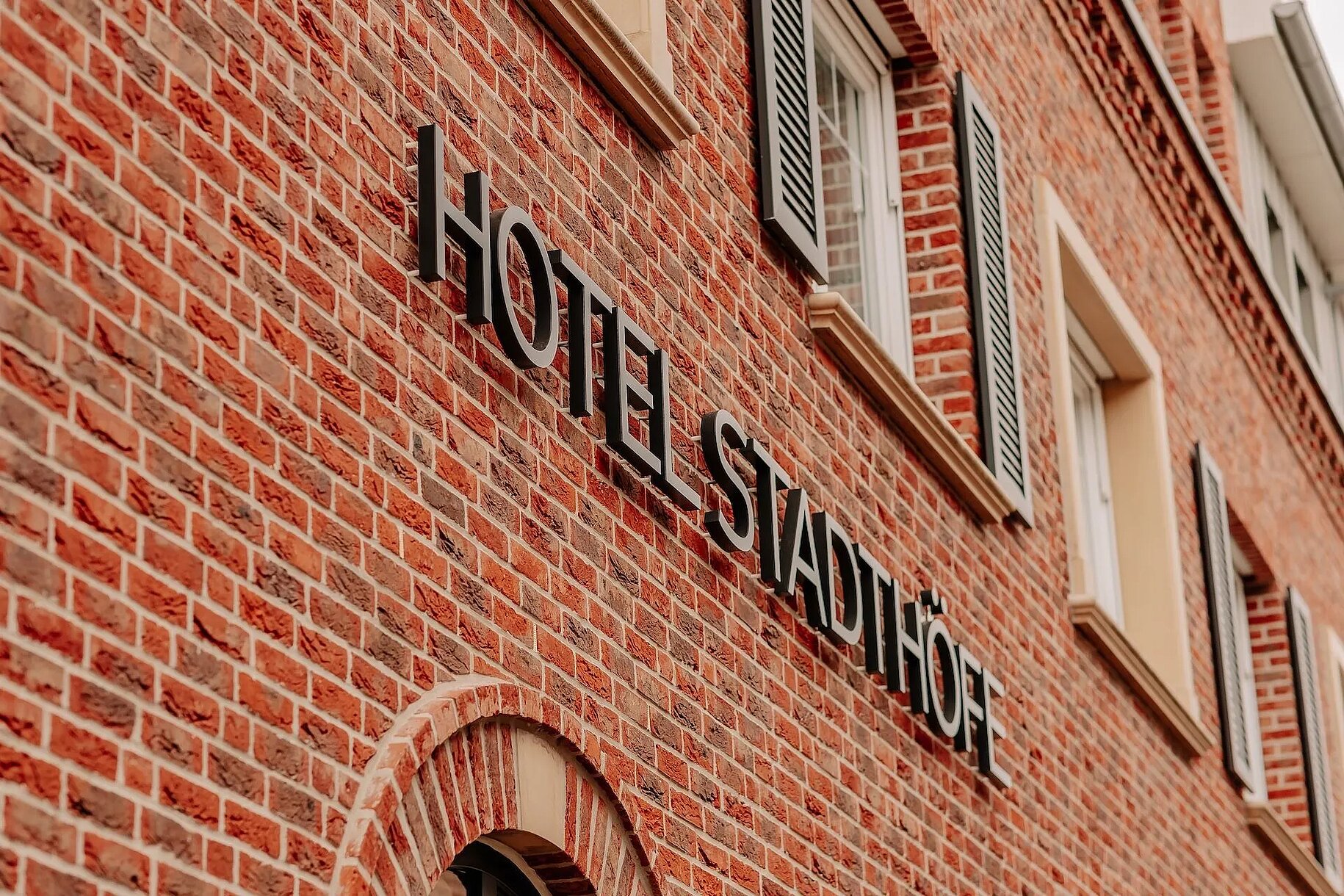 Schriftzug an der Fassade – Hotel Stadthöfe Rhede Fassadendetail mit Logo-Schriftzug des Hotel Stadthöfe Rhede auf rotem Backstein