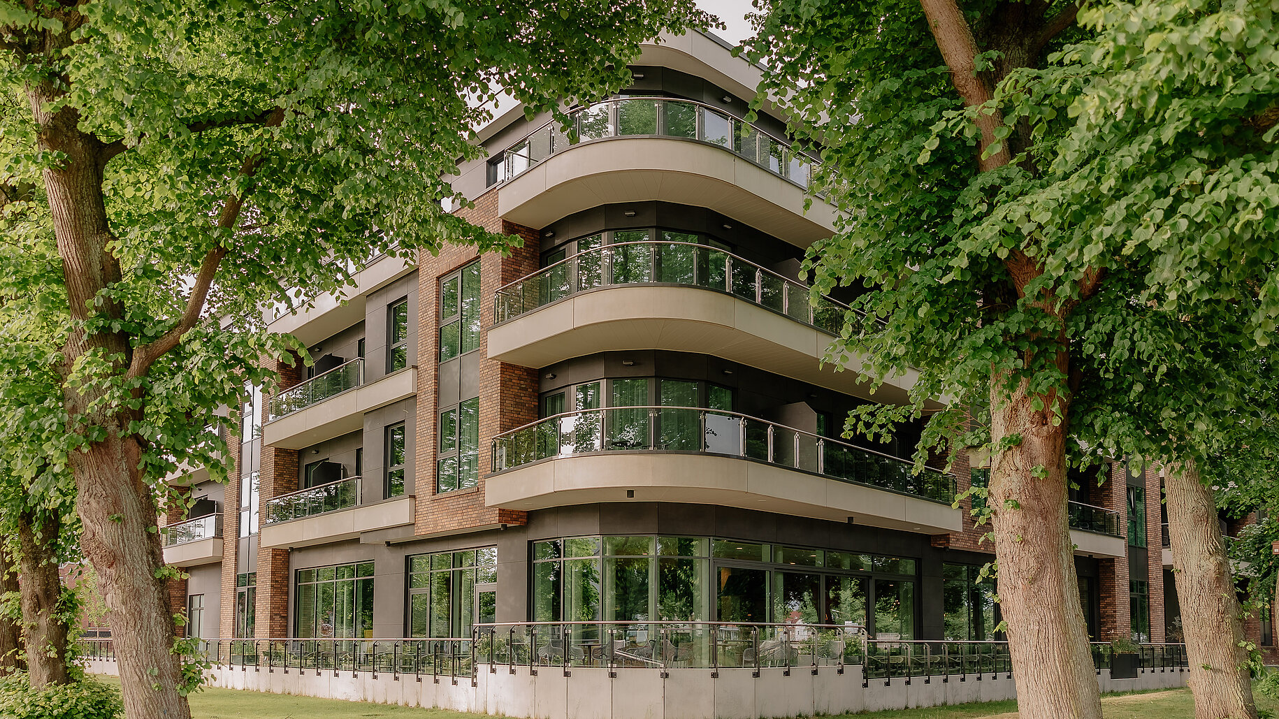 Außenansicht des Hotels im Grünen Außenansicht eines modernen Hotels mit großen Balkonen und Glasfassade, umgeben von Bäumen