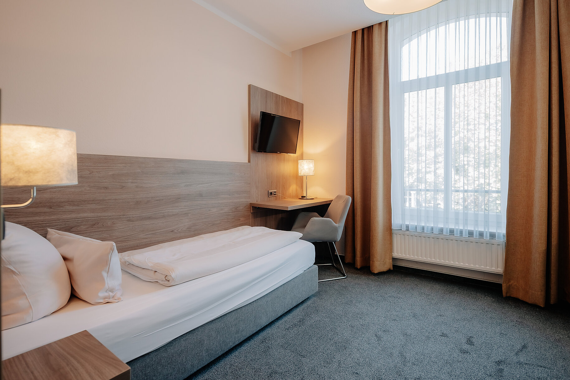 Hotelzimmer mit Arbeitsplatz Hotelzimmer mit Bett, Schreibtisch, Fernseher und großem Fenster im Parkhotel Lingen