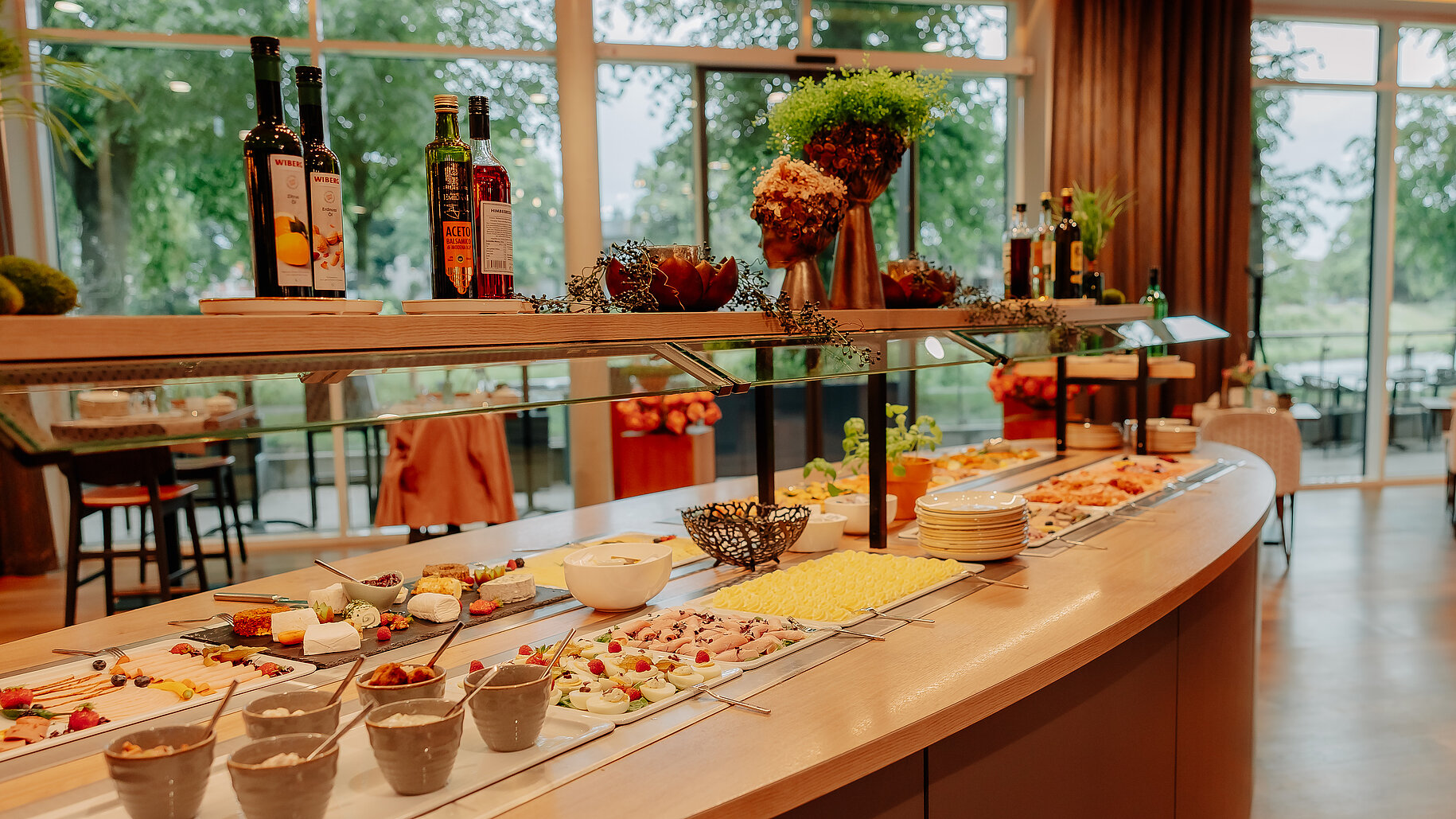 Frühstücksbuffet im Hotelrestaurant des Via Plaza in Meppen Reichhaltiges Frühstücksbuffet mit Käse, Aufschnitt, Joghurt und frischem Obst im stilvollen Restaurantbereich der Hackmann Hotels, mit Blick auf die Terrasse und viel Tageslicht