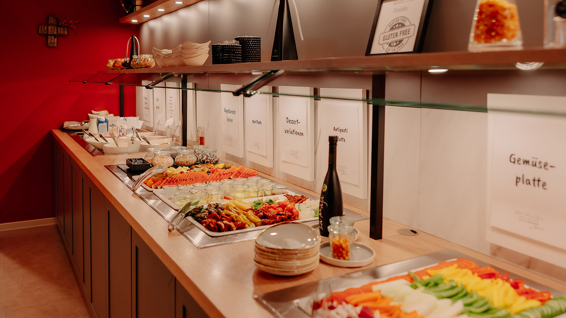 Buffet mit Gemüse- und Antipastiplatten Buntes Buffet mit Gemüseplatte, Antipasti und Dessertvariationen im Frühstücksbereich mit roter Wand